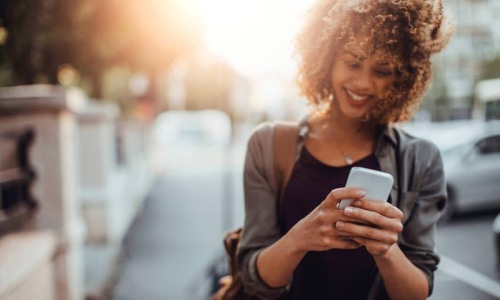 woman texts on her phone as she walks through the city